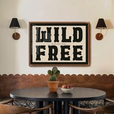 a table with two chairs and a potted plant on it in front of a framed sign that reads wild free