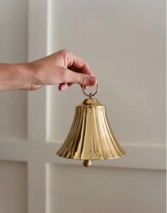 a hand holding a brass bell on a white wall