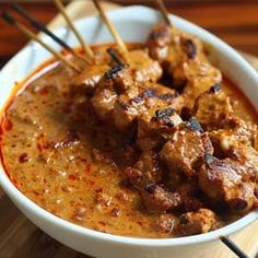 a white bowl filled with meat and chopsticks on top of a wooden table