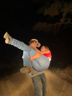 a man carrying a woman on his back in the dirt road at night with trees behind him