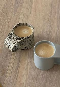 two mugs sitting on top of a wooden table next to each other, one is filled with coffee