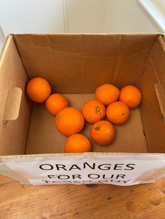 oranges in a cardboard box on a wooden table with a sign that says oranges for our family