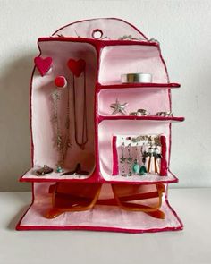 an open pink purse with jewelry in it on top of a white table and wall