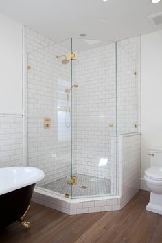 a white tiled bathroom with a black bathtub and toilet in the corner, along with a wooden floor