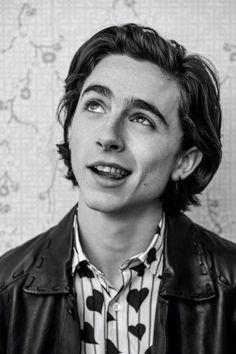 a black and white photo of a young man wearing a leather jacket with hearts on it