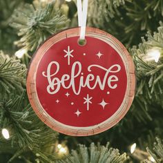 a red ornament hanging from a christmas tree with the words believe on it