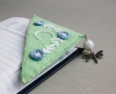 a bookmark with a green triangle and blue flowers on it sitting next to an open notebook