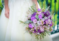 a bridal holding a bouquet of purple and white flowers on her wedding day in front of a railing