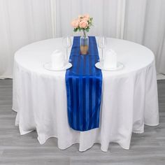 a white table topped with a blue runner and vase filled with flowers on top of it