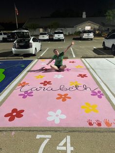 a woman kneeling on top of a parking lot with flowers painted on the ground next to her