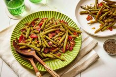 green beans and tomatoes are on a plate with a wooden spoon next to some glasses