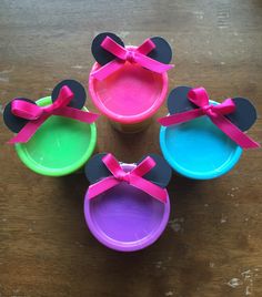 three mickey mouse shaped plastic cups with pink bows on the top and one is green