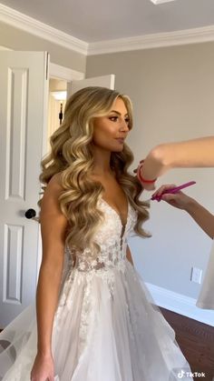 a woman in a wedding dress getting her hair done by another woman who is holding a pair of scissors