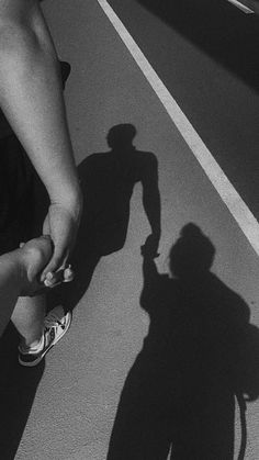 the shadow of a person holding an object in their hand while standing next to a street