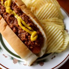 a chili dog with mustard and ketchup on a plate next to potato chips