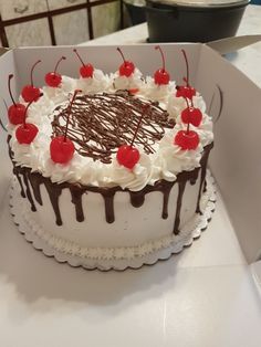 a cake with white frosting and cherries on the top is in a box