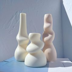 three white vases sitting next to each other on top of a blue countertop