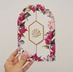 a person holding up a card with flowers on it and an arabic calligraphy in the middle