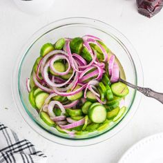 a glass bowl filled with sliced onions and cucumbers on top of a white table