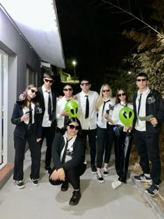 a group of people standing next to each other wearing sunglasses and holding green heart shaped balloons