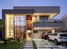 two cars are parked in front of a modern house at night with lights on the windows