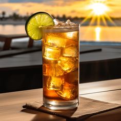 a tall glass filled with ice and lime on top of a wooden table next to water