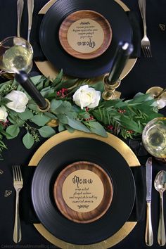 the table is set with black and gold plates, silverware, and greenery