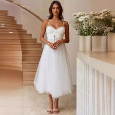 a woman in a white dress standing next to some stairs with flowers on the floor