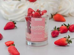 a glass filled with strawberries on top of a white table next to whipped cream