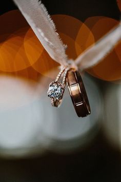 two wedding rings are attached to a feather with lights in the back ground behind them