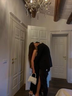 a man and woman kissing in a room with chandelier hanging from the ceiling