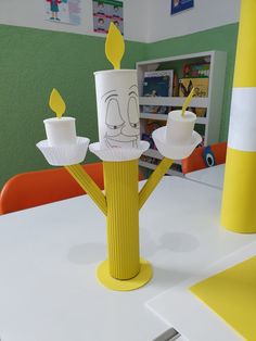 a yellow vase with two candles in it sitting on a table next to a cupcake holder