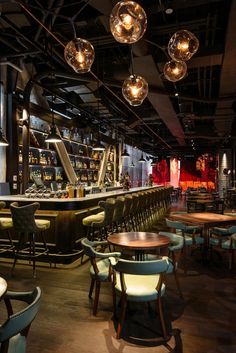 an empty bar with lots of chairs and lights hanging from the ceiling, along with several tables