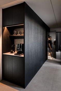 a kitchen area with black cabinets and counter tops, while a woman is in the background