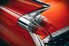 the taillight of an old red car with chrome trim and hood ornament