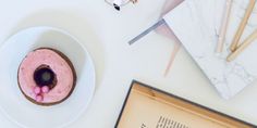 a pink frosted donut sitting on top of a white plate next to an open book