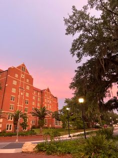 the building is red and has many trees in front of it at sunset or dawn