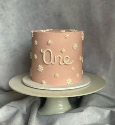 a pink cake with daisies and the word one on it sitting on a plate