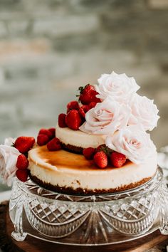 a cake with strawberries on top is sitting on a glass platter and has white frosting