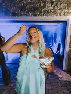 a woman in a blue dress is holding a spoon and eating something out of a bowl