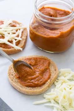 a jar of red sauce next to two slices of bread with cheese on it and a spoon