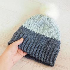 a hand is pointing at a knitted hat with a pom - pom