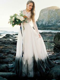 a woman in a white and black wedding dress standing on rocks near the ocean with flowers