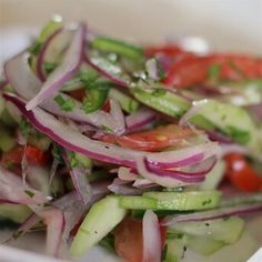 a salad with red onions, cucumbers and tomatoes in it on a white plate