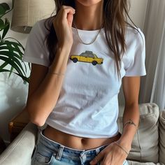 Embrace nostalgic vibes with our Retro Embroidered Taxi Baby Tee! This aesthetic cropped T-shirt features a charming NYC taxi design, perfect for a cool girl outfit. Ideal for those who love trendy vintage tops, this graphic tee gives a refined and elevated look. It is the perfect gift for a loved one, or as a treat for yourself. Inspired by the timeless 90s vintage look, our baby tees are slightly more fitted and cropped than regular t-shirts, highlighting a flattering and fashionable silhouette. Available in sizes S, M, L, and XL, this tee is designed to suit every figure beautifully, and is both trendy and timeless Please consult the size chart before making your purchase. Due to the custom nature of our products, we regret that we cannot accept returns or exchanges at this time. Howeve Casual White Cropped T-shirt With Funny Print, Trendy Crew Neck Top With Front Print, Summer Cropped T-shirt With Funny Print And Crew Neck, Casual Summer T-shirt With Embroidered Graphics, Trendy Embroidered Crew Neck T-shirt, Basic Crew Neck Top With Front Print, Fitted Summer Tops With Embroidered Graphics, Funny Print Cropped Cotton T-shirt, Summer Embroidered Graphic Tee