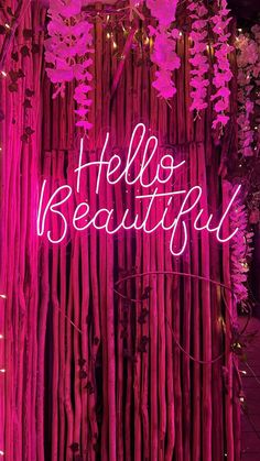 a pink neon sign that says hello beautiful in front of bamboo stalks and trees with purple flowers