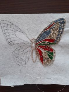 an embroidered butterfly sitting on top of a piece of white paper with beading around it