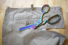 a pair of scissors sitting on top of a piece of cloth next to a pair of pants