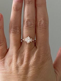 a woman's hand with an engagement ring on top of her left hand and the middle finger