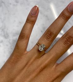 a woman's hand with a diamond ring on top of her left hand and a marble background